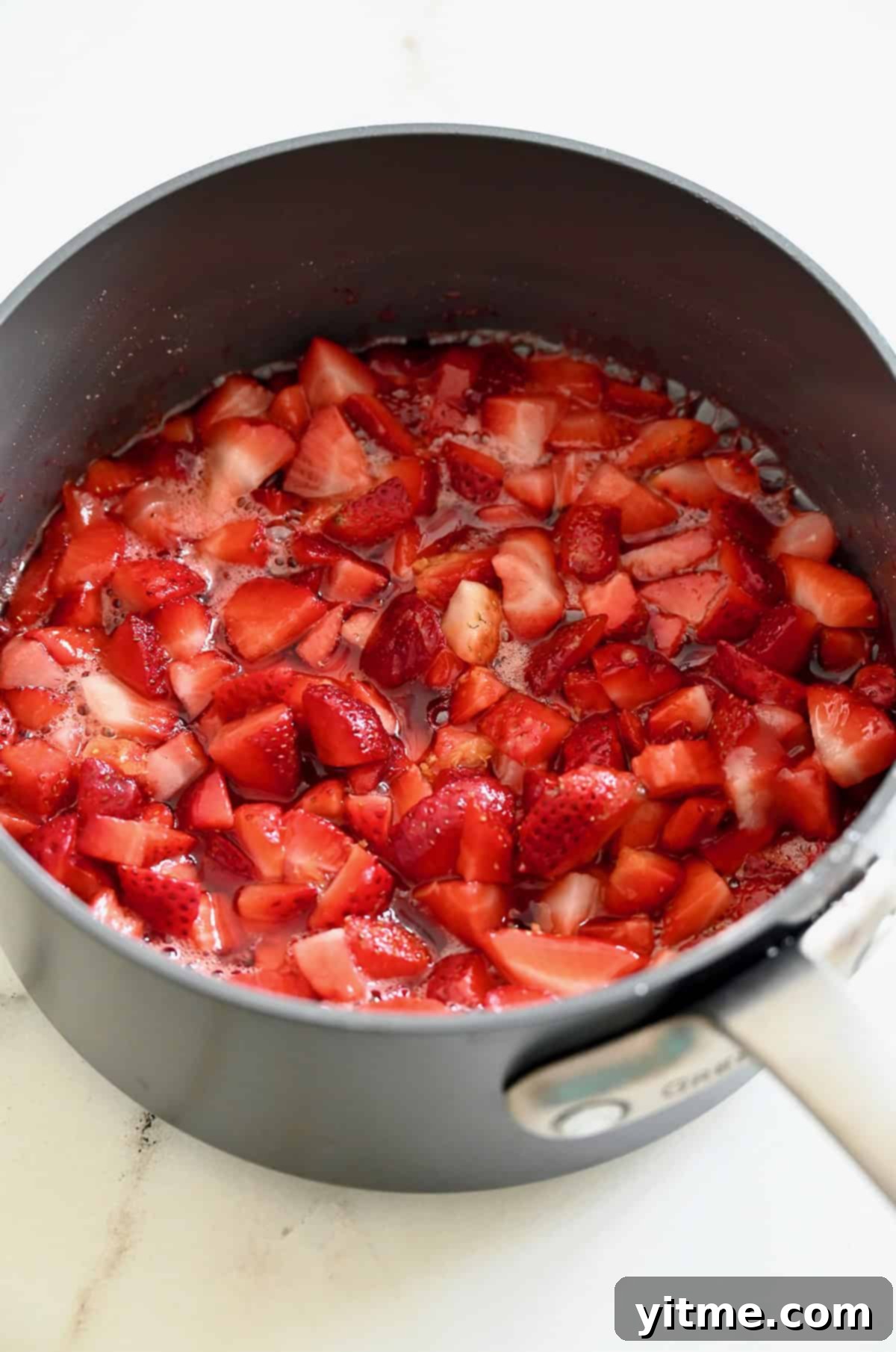 Diced strawberries simmering in a saucepan with sugar, lemon juice and lemon zest, creating a delicious homemade sauce.