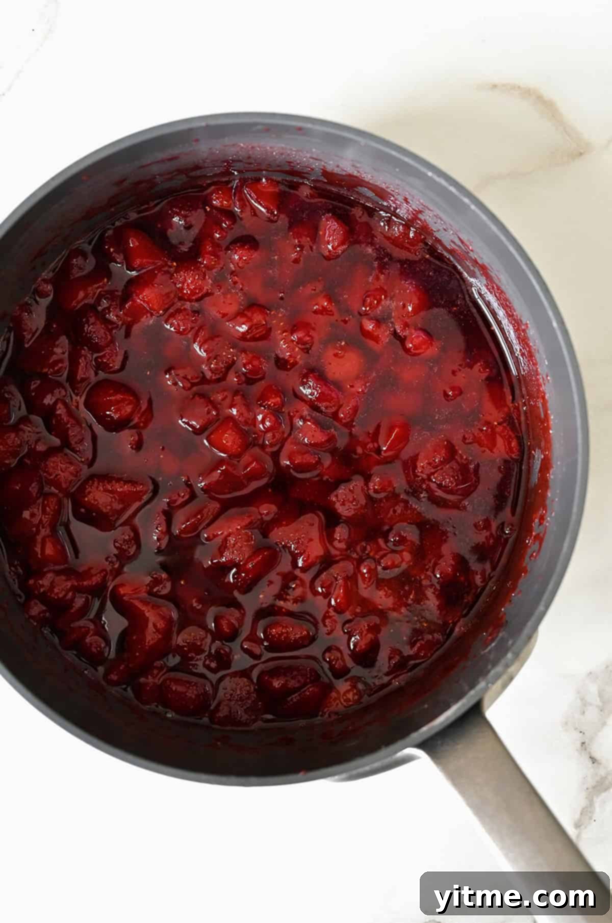 Homemade strawberry syrup simmering in a saucepan.