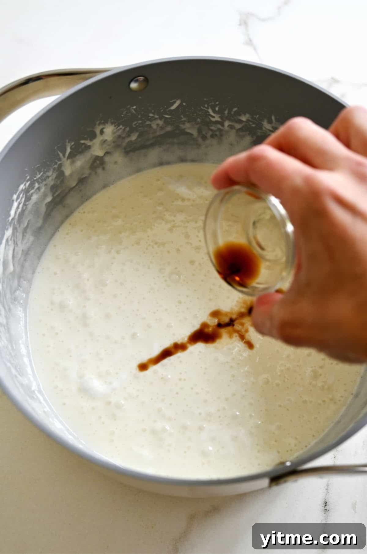 Adding vanilla to a large stockpot containing a melted butter and marshmallow mixture.