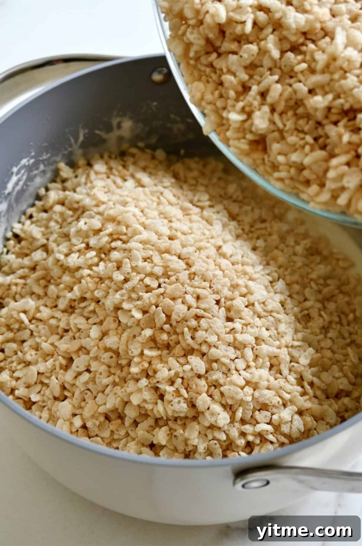 Adding Rice Krispies cereal to a stockpot containing a mixture of melted marshmallows and butter.