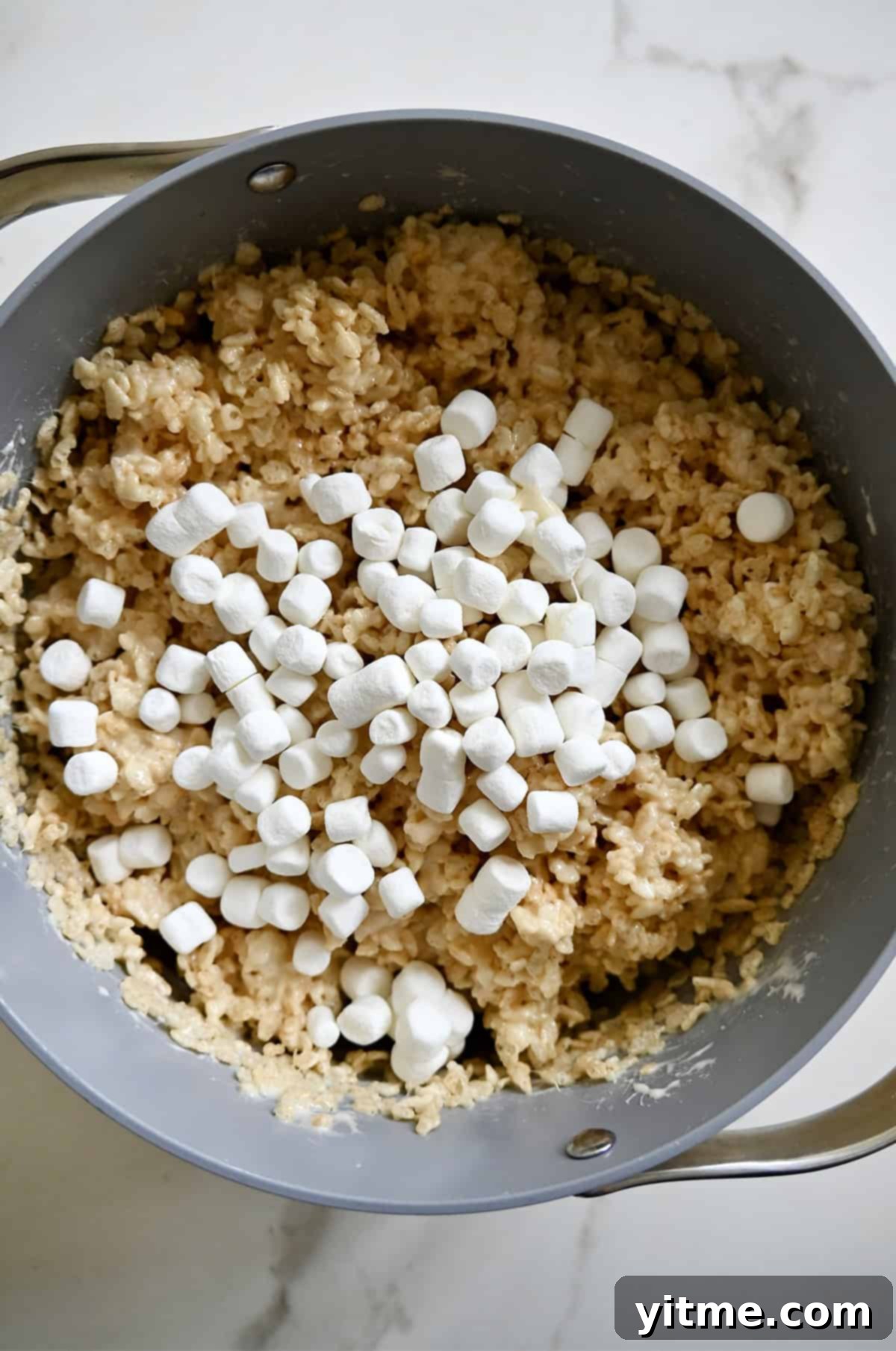 Adding mini marshmallows to a crispy treats mixture in a stockpot.