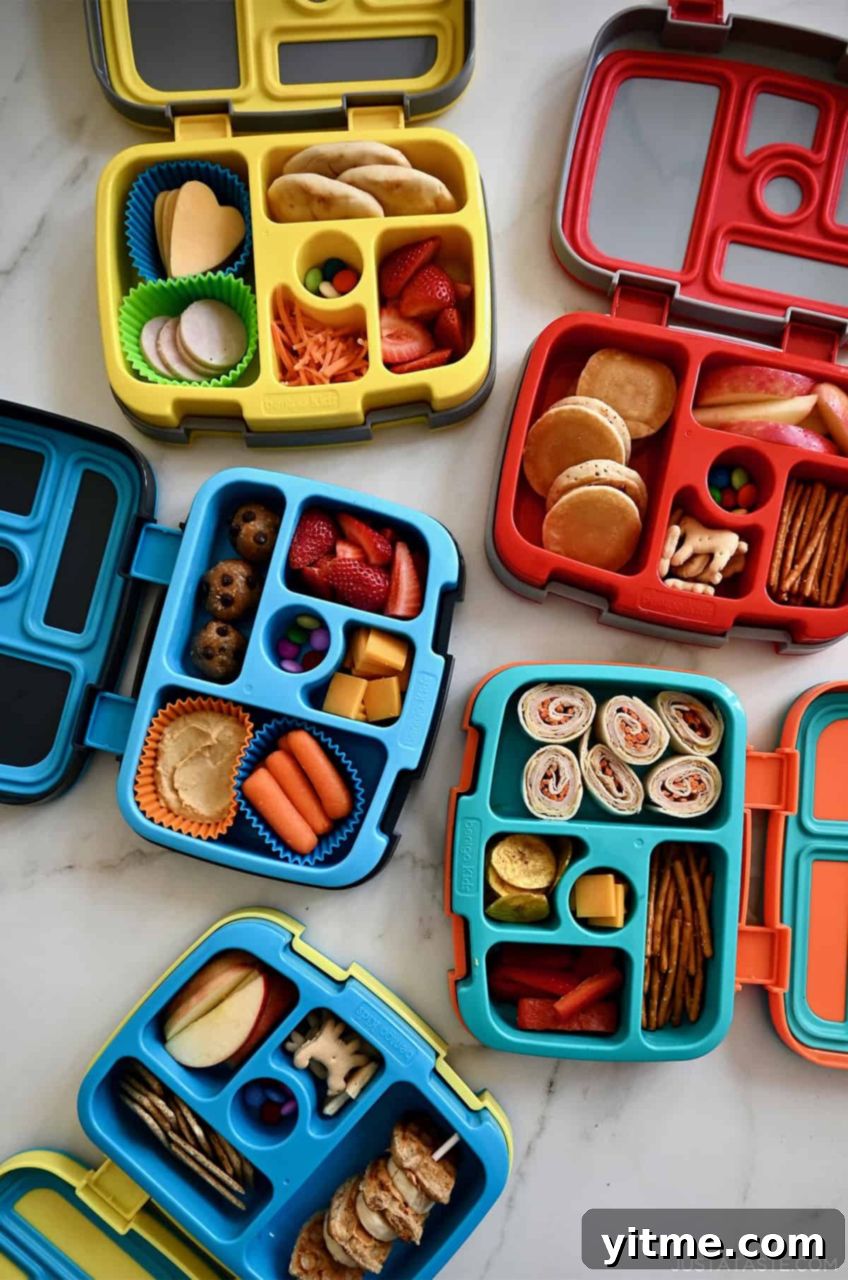 Four Bentgo lunchboxes with fresh fruits and veggies, pinwheel sandwiches, mini pancakes, protein balls and French toast skewers.