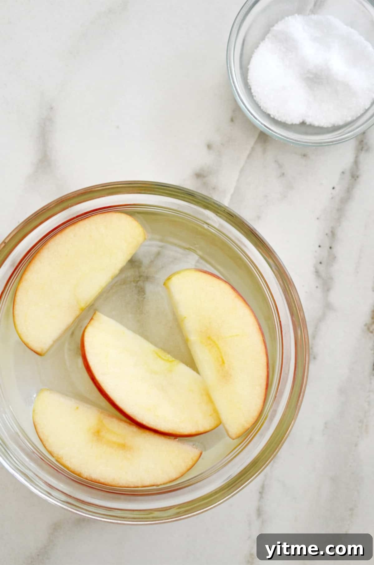 Freshly cut apple slices gently soaking in a clear bowl of saltwater solution, showing a key step in preventing browning.
