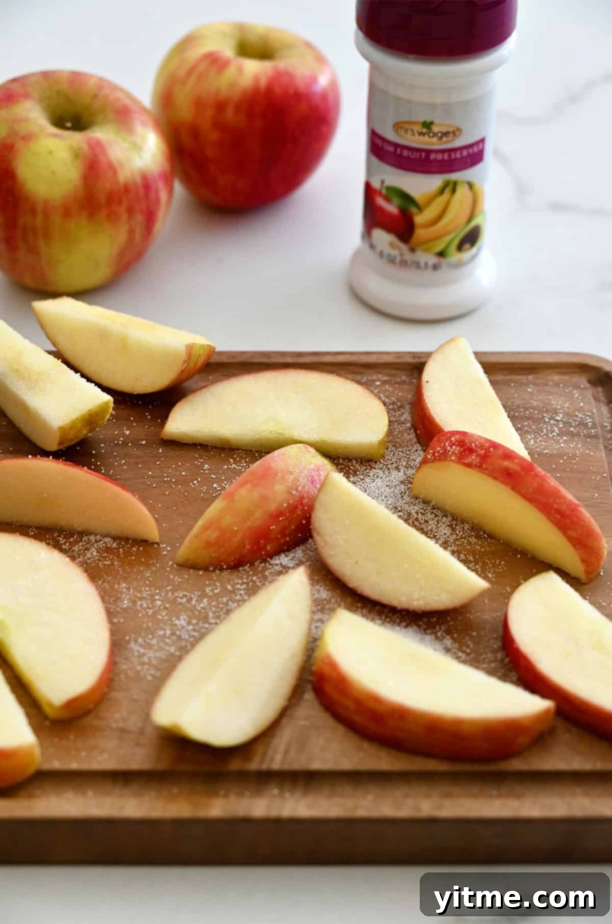 Apple slices neatly arranged on a cutting board, lightly sprinkled with a commercial fruit preserver powder.