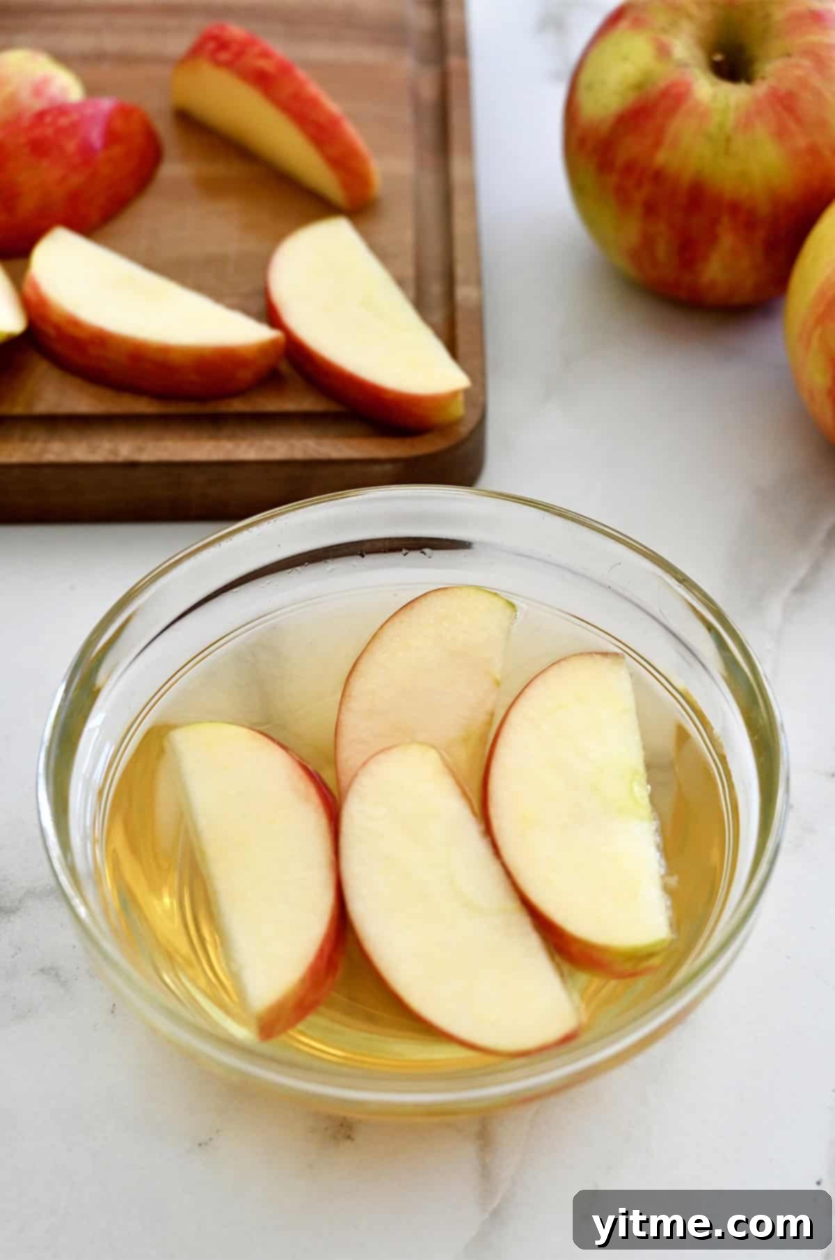 A small glass bowl containing apple slices soaking in apple cider vinegar, prepared for a browning prevention test.