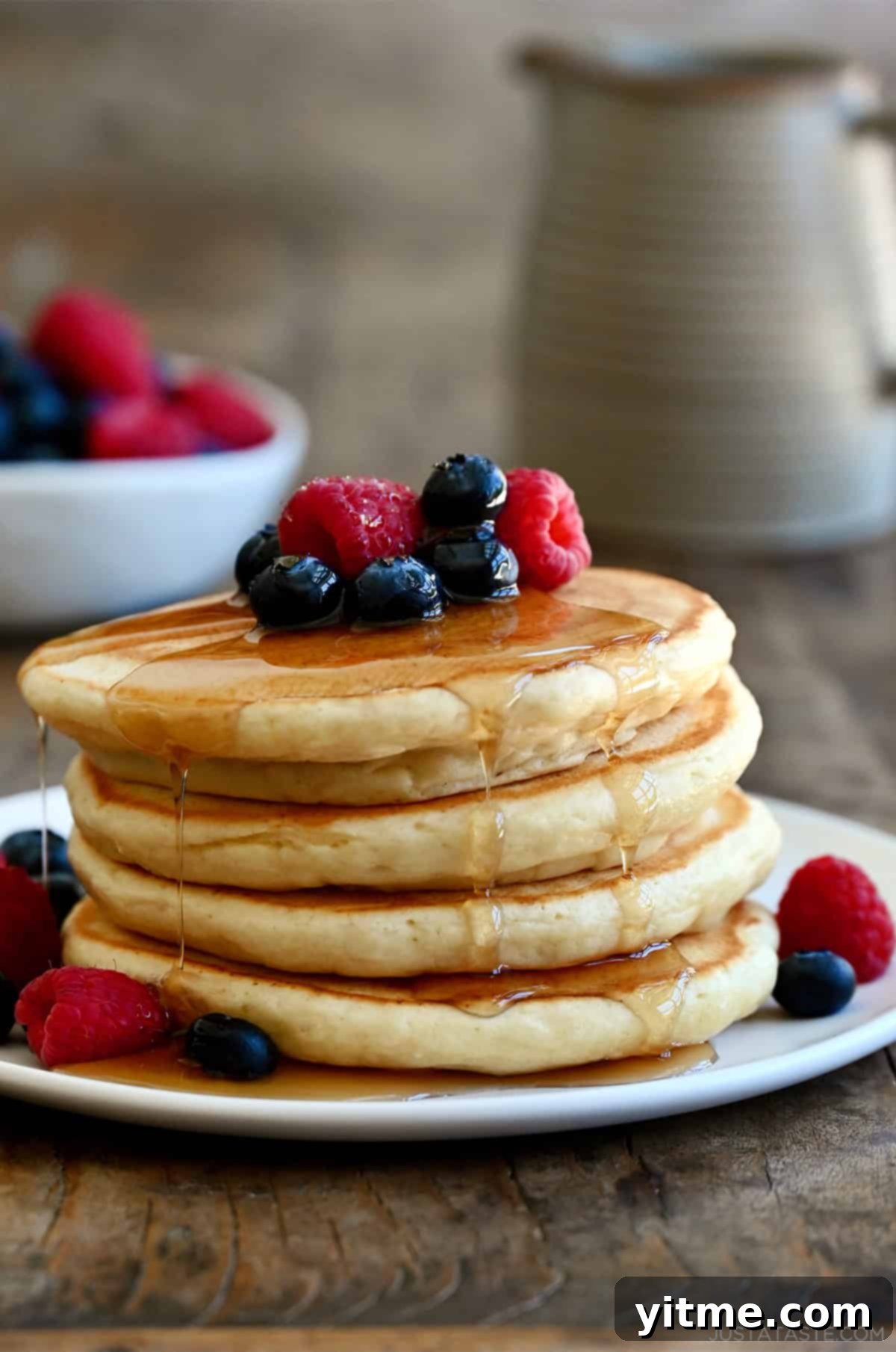 Cloud-Like Cottage Cheese Pancakes 2 A delightful stack of cottage cheese pancakes on a white plate, generously topped with fresh fruit and drizzled with sweet syrup.