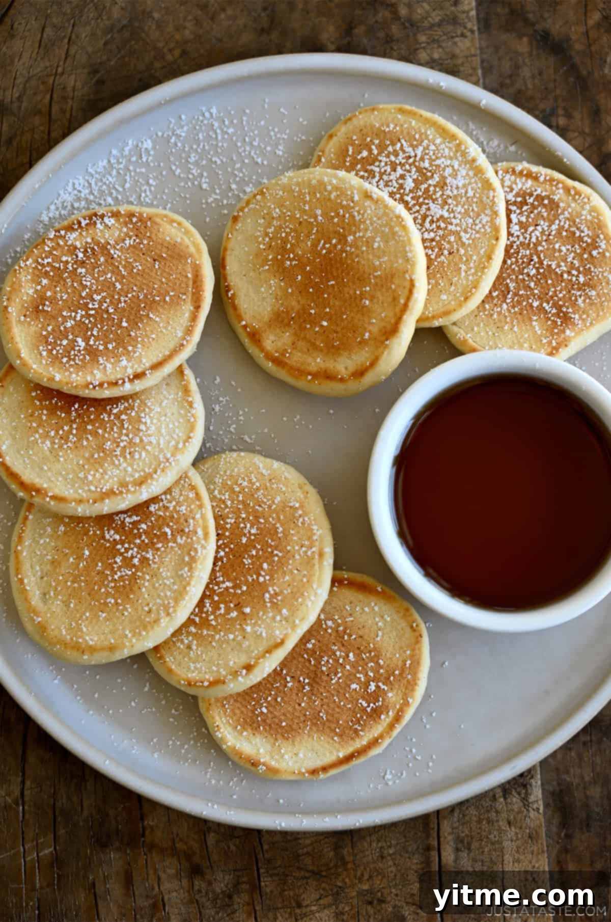 Cloud-Like Cottage Cheese Pancakes 11 A plate of adorable silver dollar-sized cottage cheese pancakes, lightly dusted with powdered sugar and served with a side of syrup.