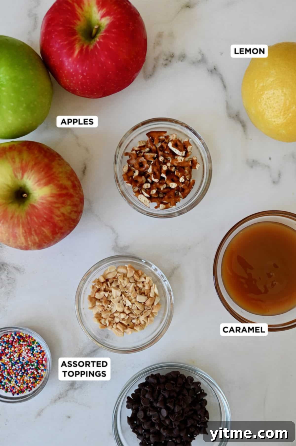 Ingredients for apple nachos: apples, caramel sauce, sprinkles, crushed peanuts, crushed pretzels, mini chocolate chips, and a lemon.