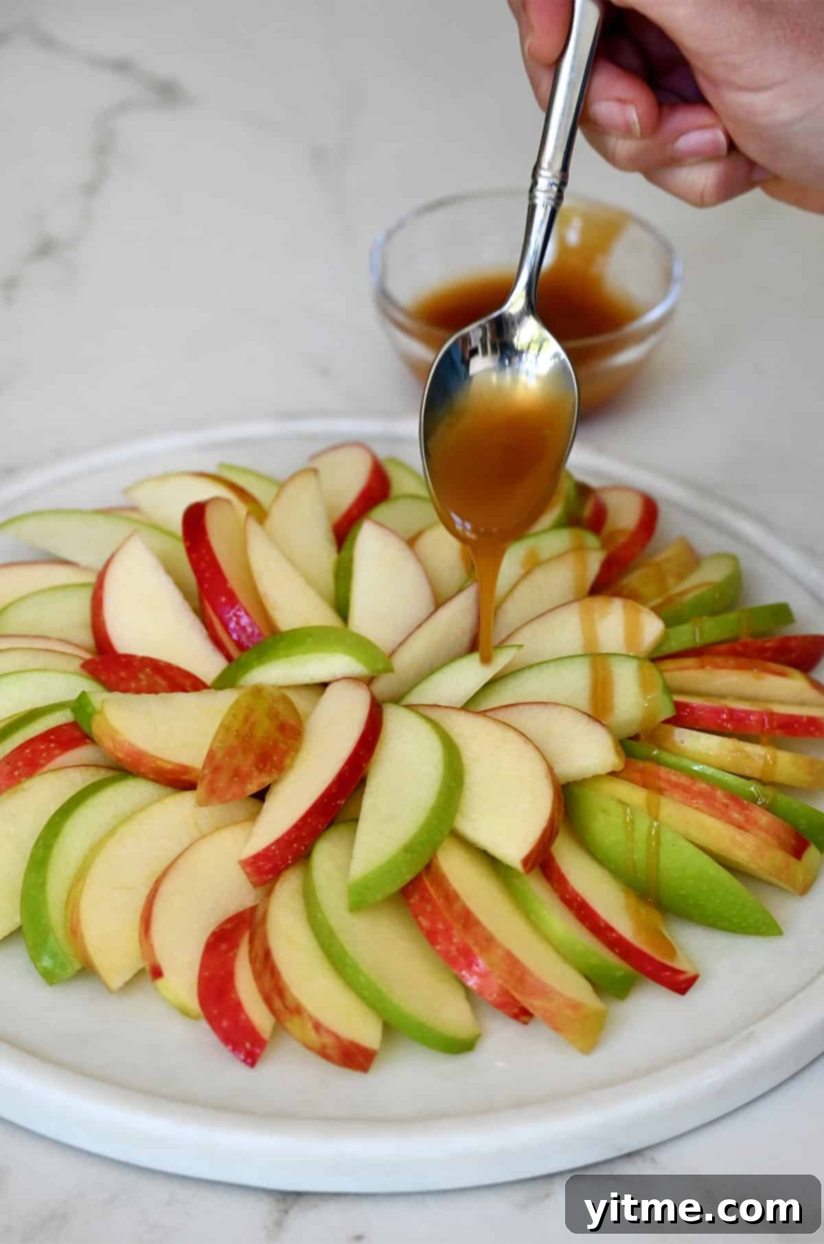 Drizzling caramel over apple slices on a serving platter.