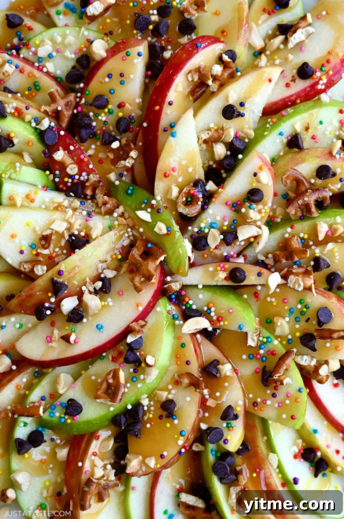 Apple nachos with red and green apple slices, caramel drizzle, chocolate chips, peanuts, sprinkles, and pretzels.