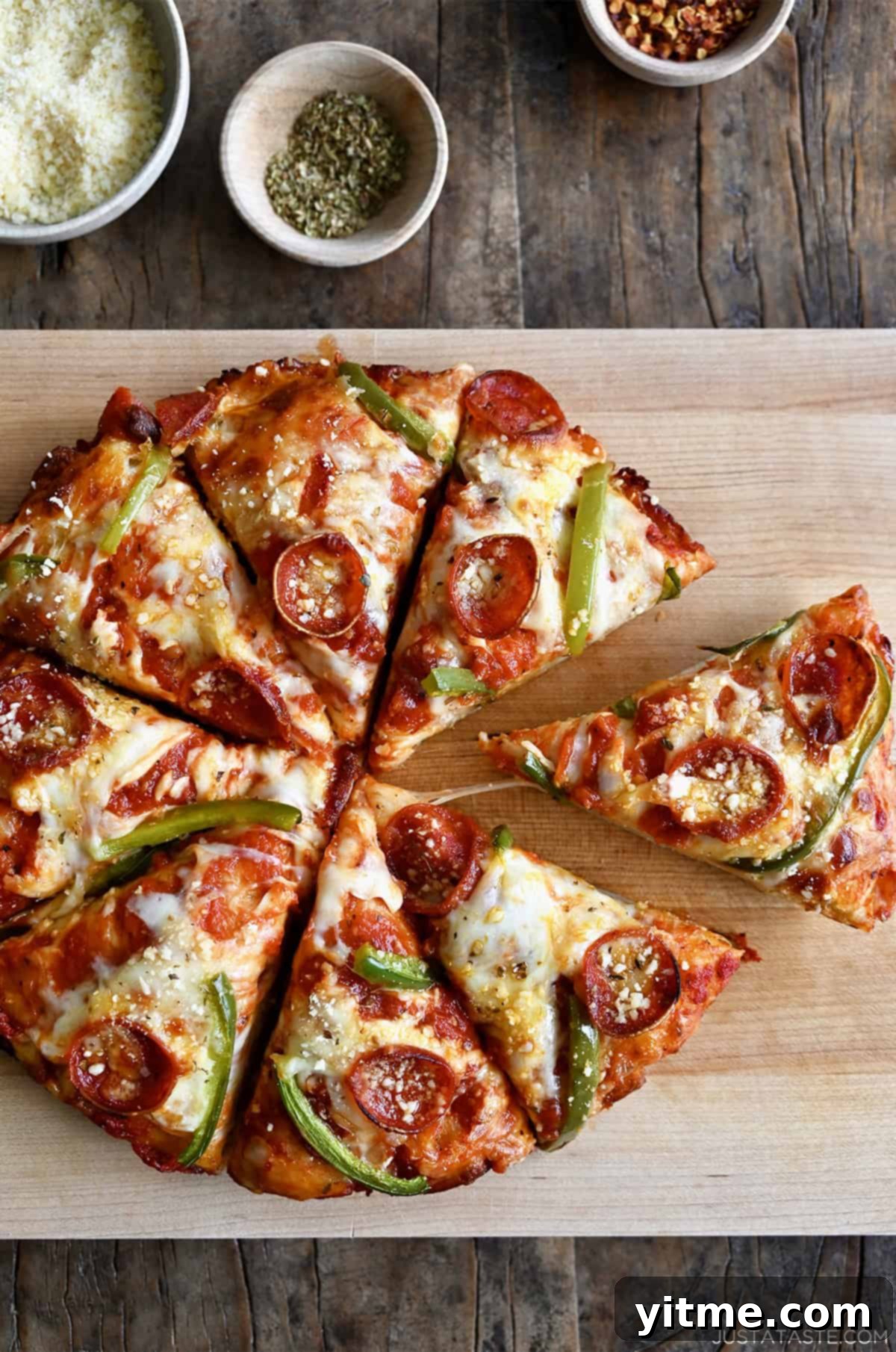 Cast iron pizza with pepperoni, green peppers, and plenty of cheese, cut into eight slices on a wooden cutting board.