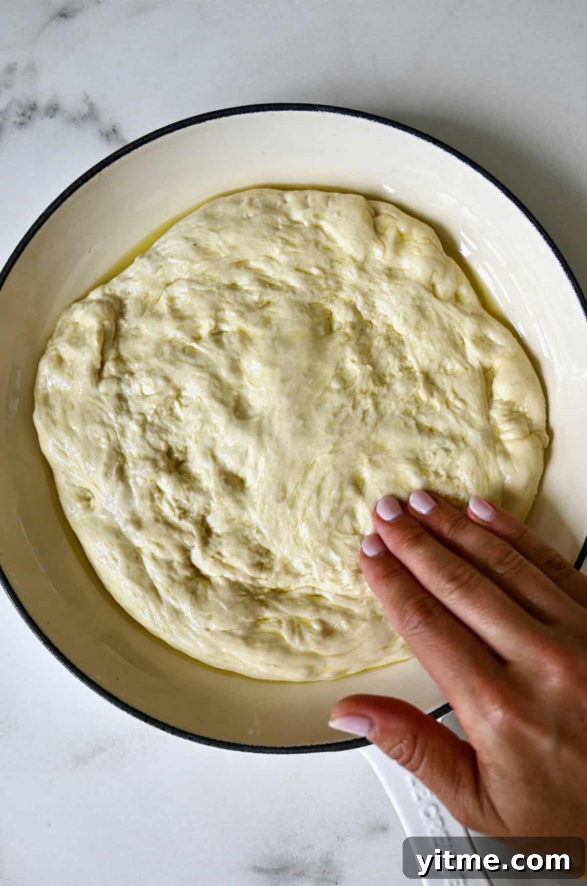Pizza dough ball placed in a skillet with olive oil, being turned once to coat, then gently pressed out to the edges of the pan.