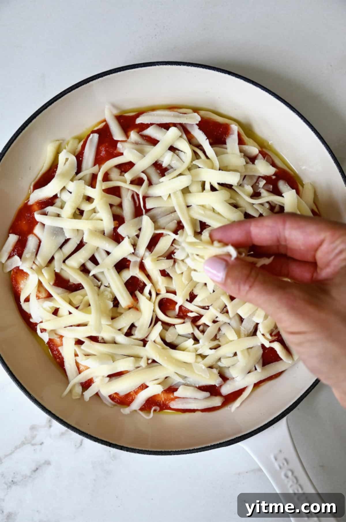 Adding a generous layer of shredded mozzarella cheese on top of pan pizza dough, already coated with marinara sauce, for optimal melt.