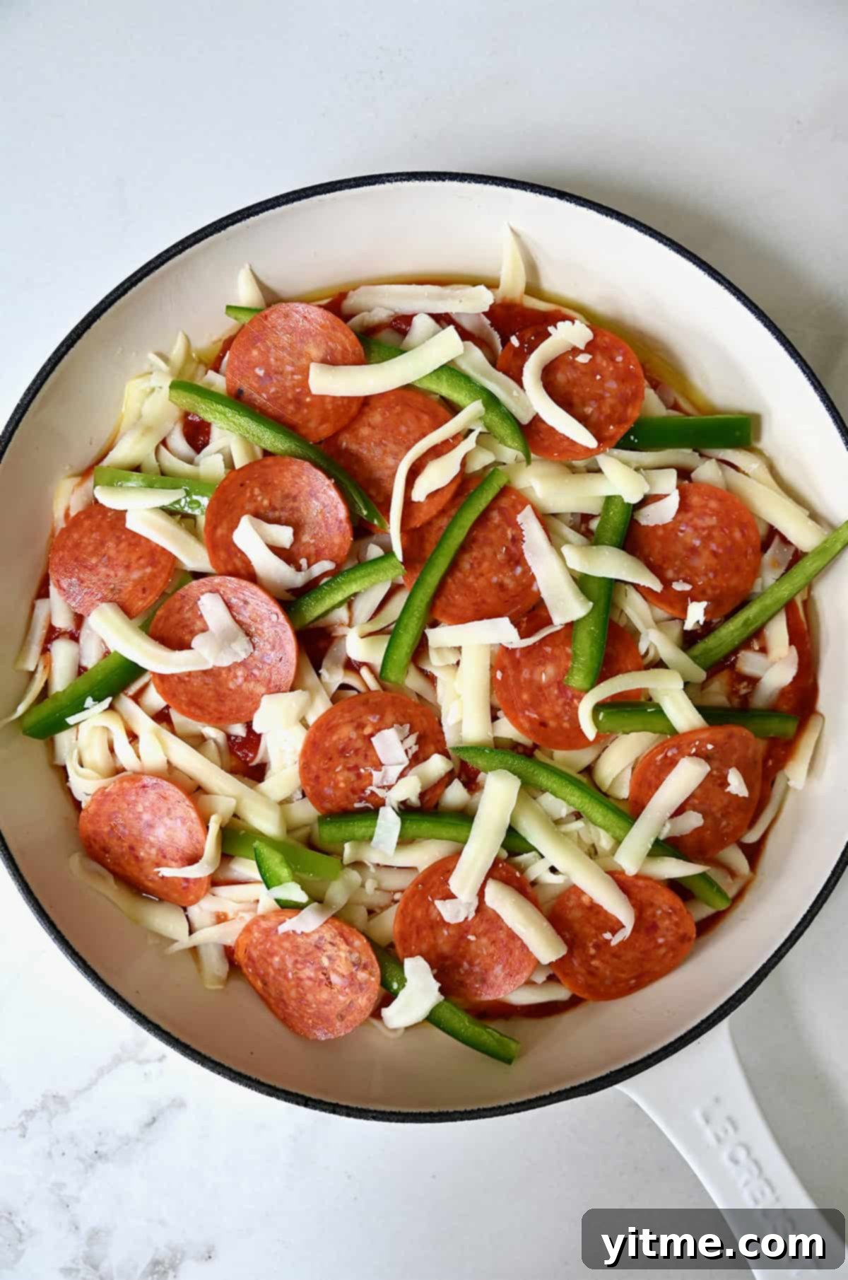 Adding colorful pizza toppings, including classic pepperoni slices and vibrant sliced green peppers, atop an unbaked pan pizza in a skillet.
