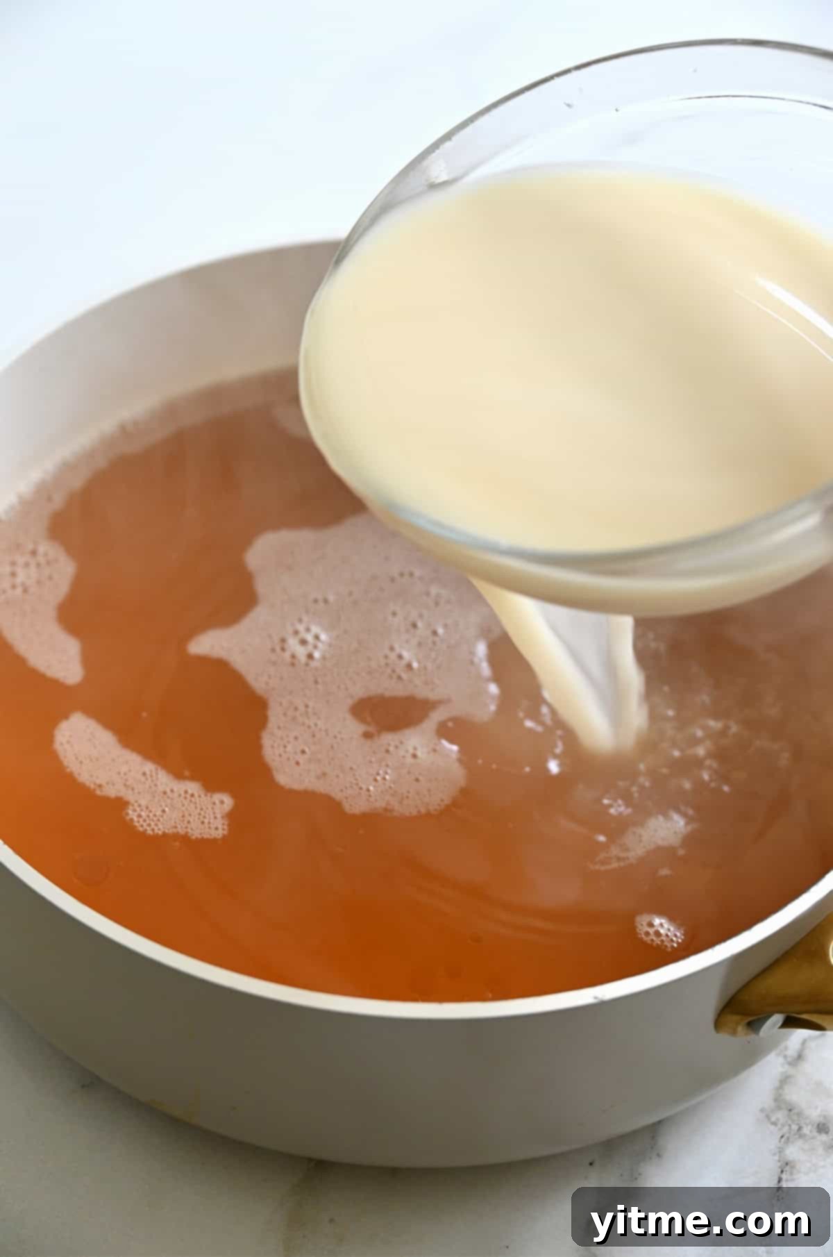 A cornstarch slurry is slowly poured into the boiling broth in a stock pot, being continuously whisked.