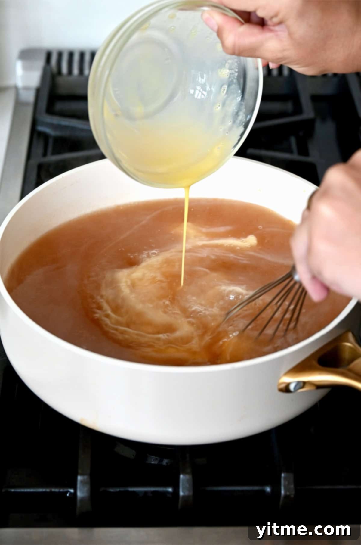 Beaten eggs are carefully drizzled into a pot of hot, simmering egg drop soup broth while being whisked to create delicate egg ribbons.