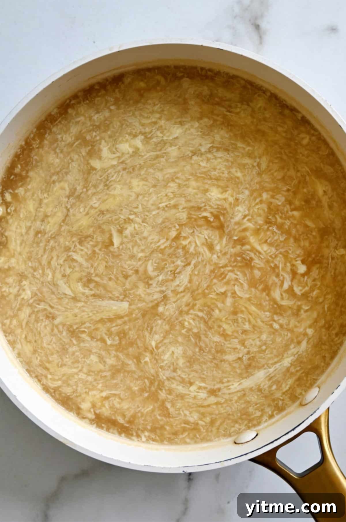 A close-up of a stock pot filled with freshly made homemade egg drop soup, showing the clear, golden broth and fluffy egg ribbons.