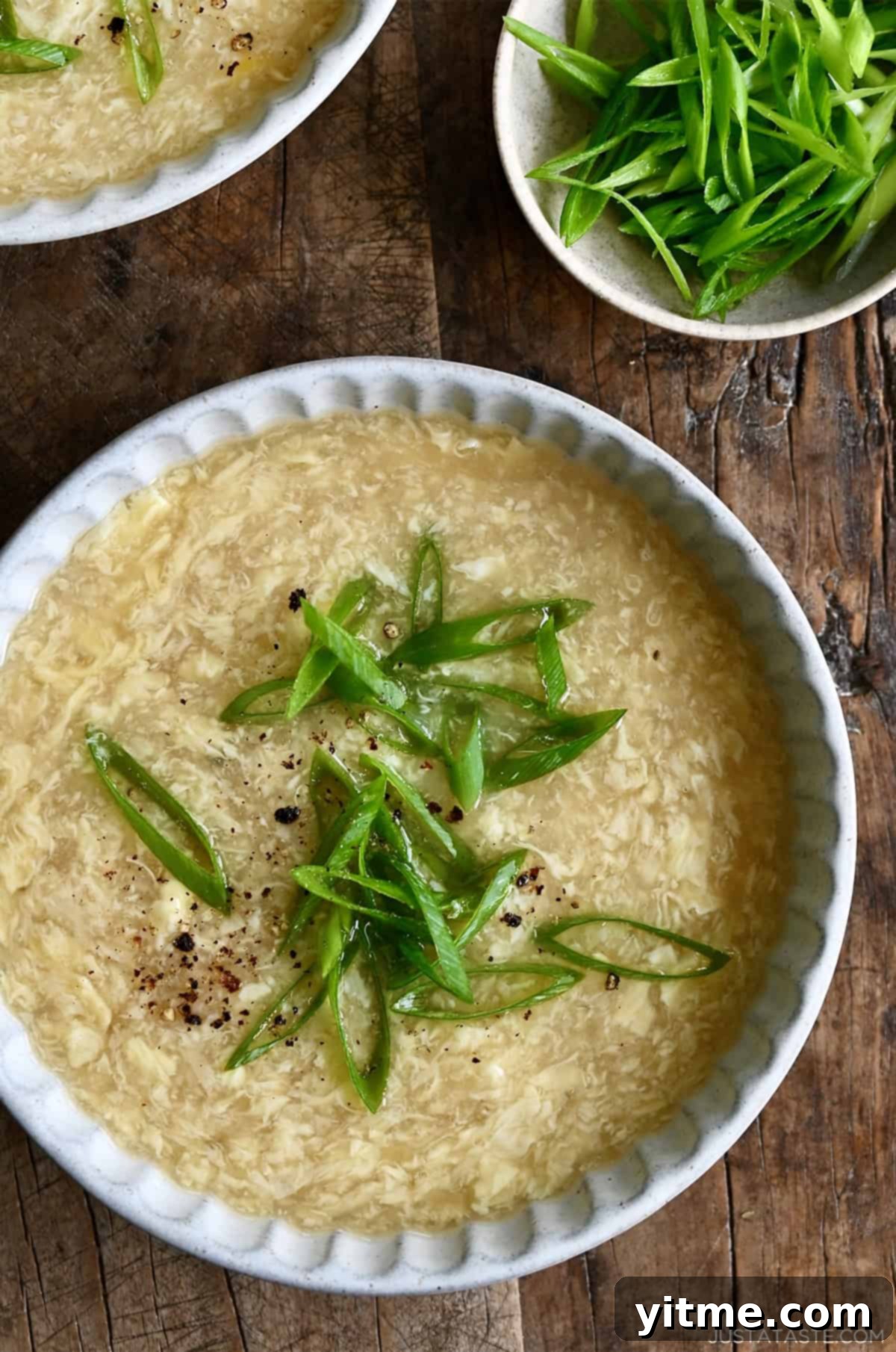 A close-up of a single bowl of homemade egg drop soup garnished with fresh scallions, highlighting the fluffy egg ribbons against a golden, clear broth.