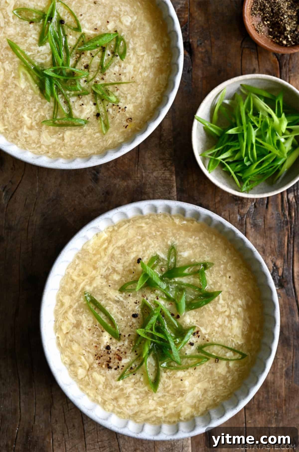 Two bowls of homemade egg drop soup topped with chopped scallions.