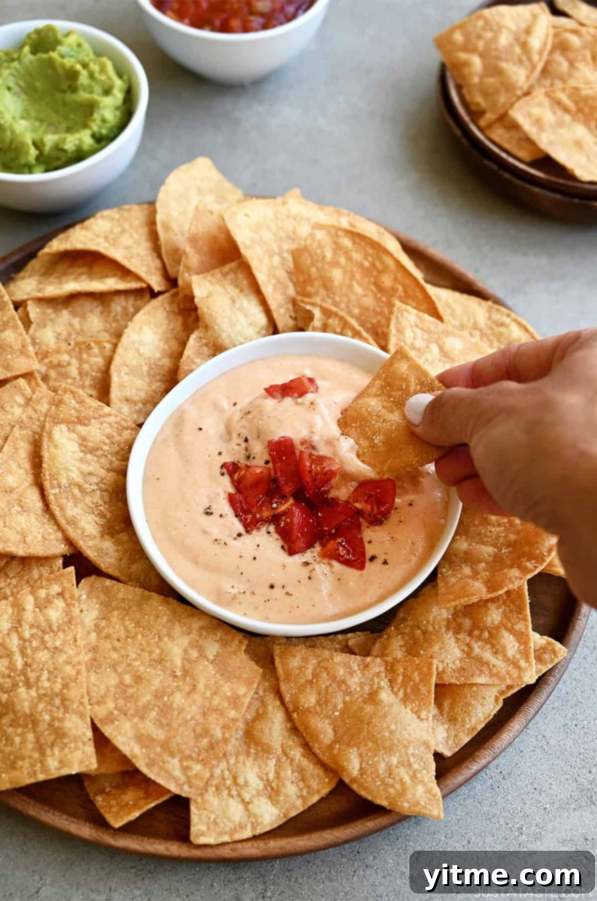 High-protein cottage cheese queso dip in a bowl topped with roasted tomatoes and black pepper on a plate surrounded by tortilla chips.
