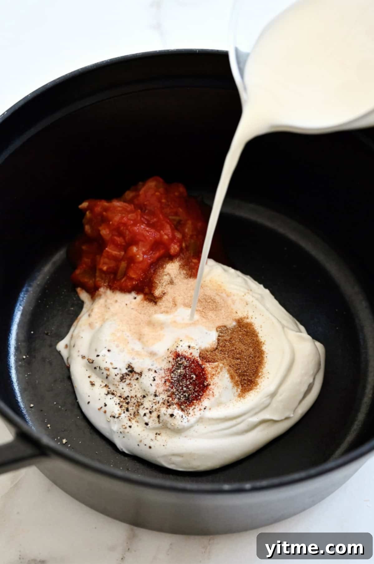 Milk being poured over blended cottage cheese, salsa and taco seasonings in a saucepan.