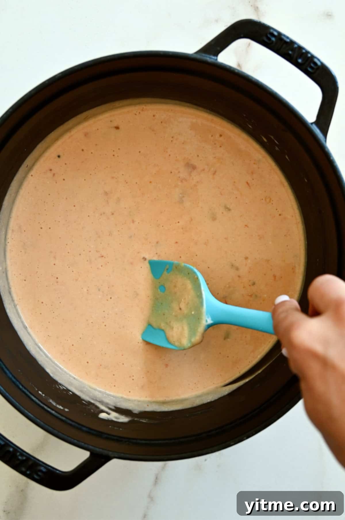 Extra-creamy cottage cheese queso dip in a saucepan being stirred with a teal spatula.