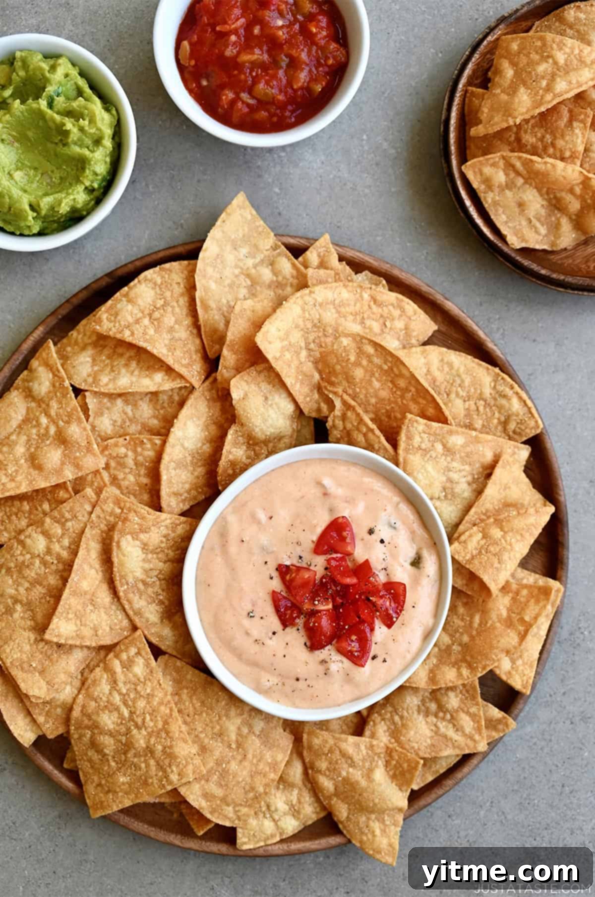 Warm homemade cottage cheese queso in a bowl topped with chopped tomatoes on a plate surrounded by tortilla chips.