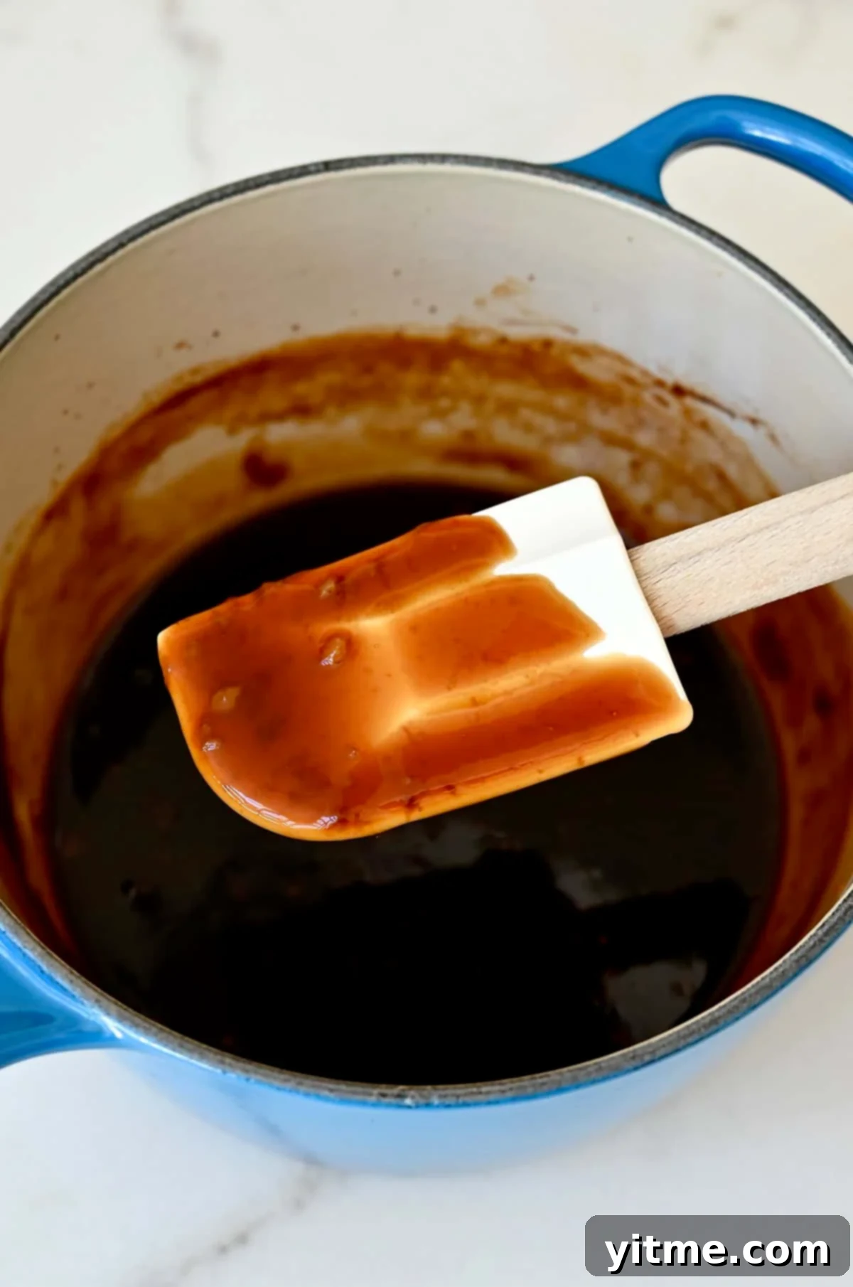 A spatula coated in easy homemade teriyaki sauce above a saucepan with sauce, showcasing its thick and glossy texture.