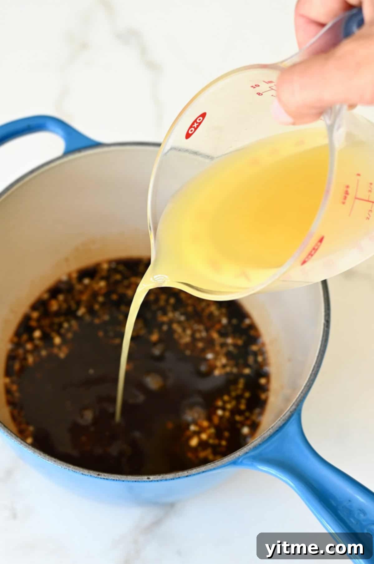 Pouring pineapple juice into a saucepan with soy sauce, brown sugar, minced garlic, and ginger, initiating the teriyaki sauce base.