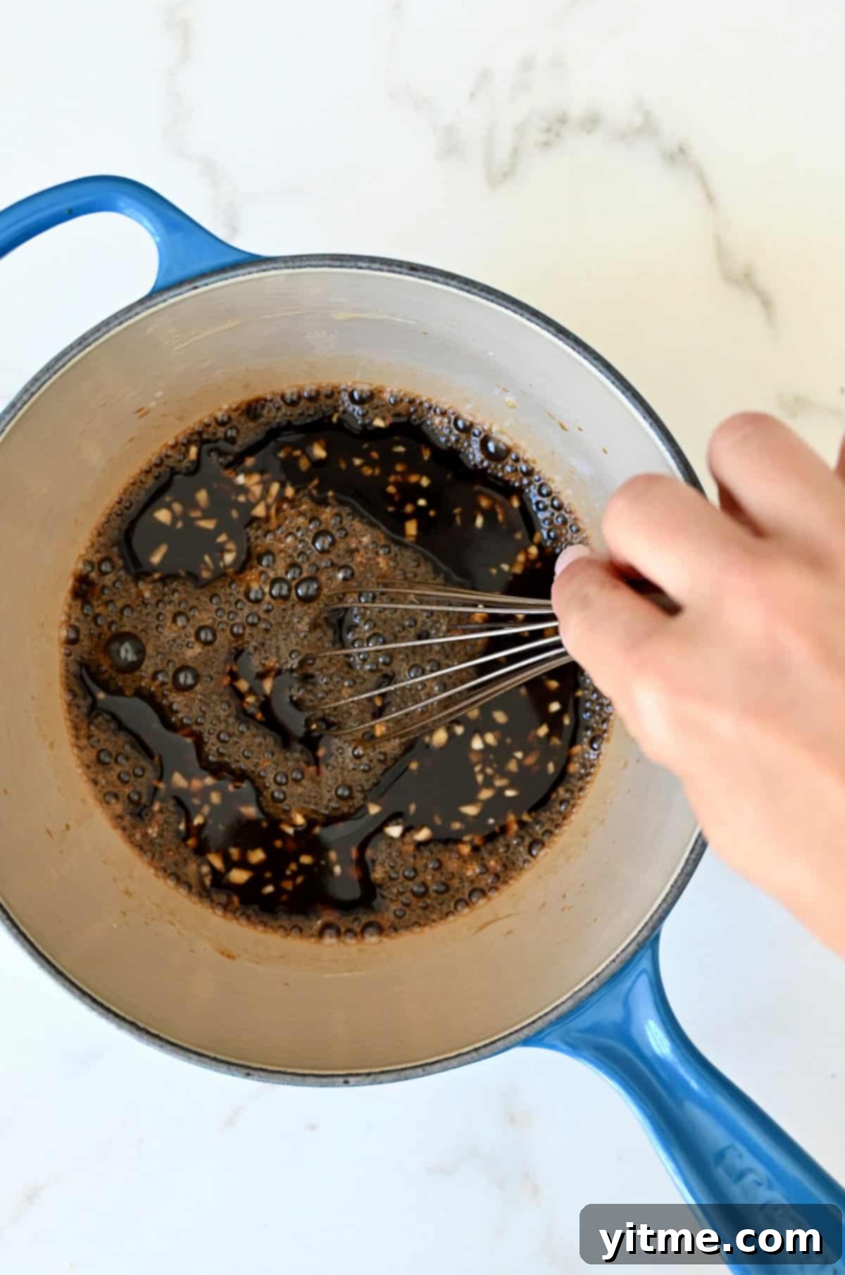 Whisking teriyaki sauce ingredients together in a saucepan on the stove, ensuring smooth consistency.