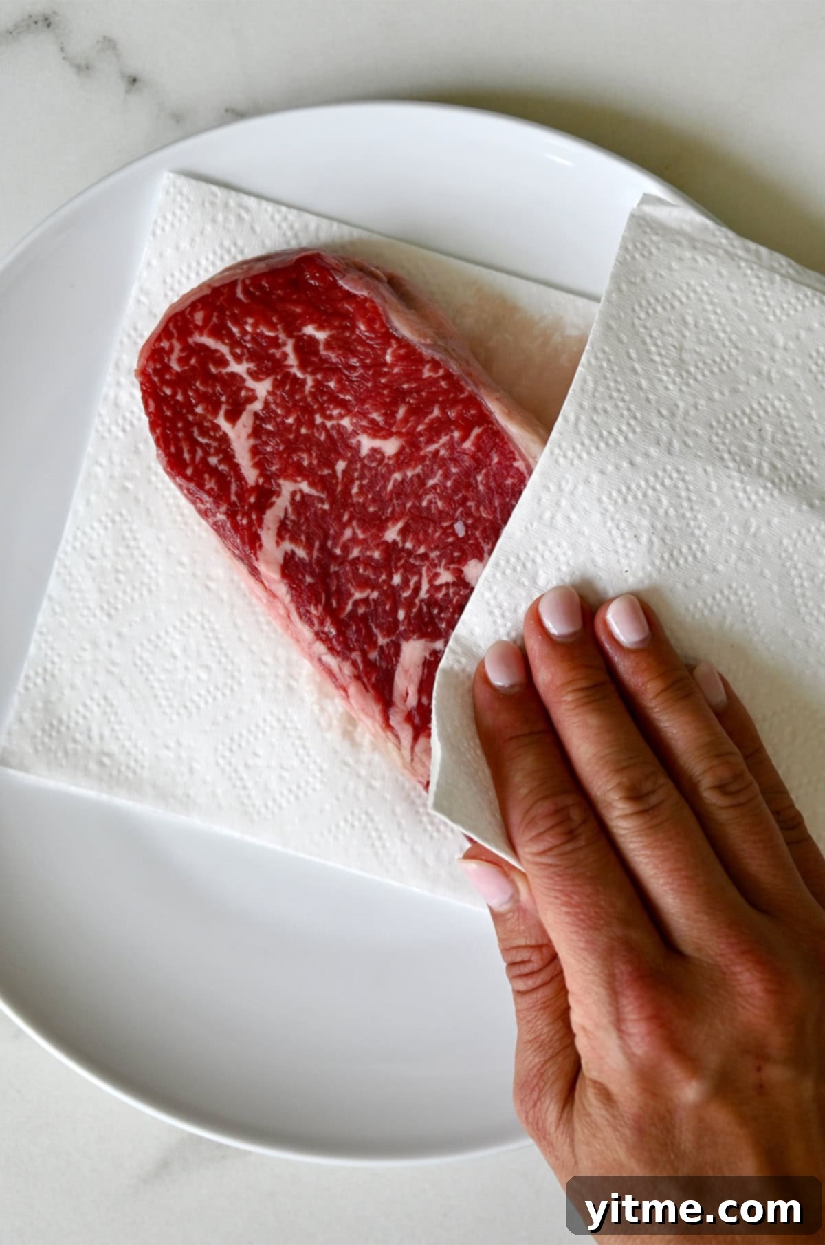 Patting a steak dry with a paper towel to ensure optimal searing and crust formation.