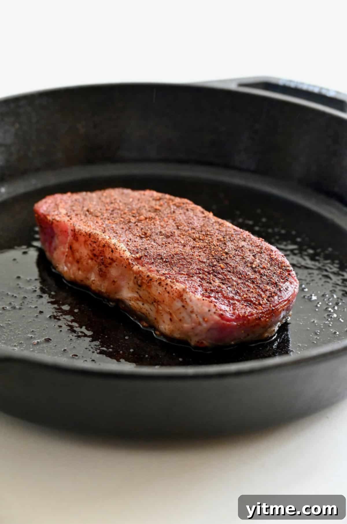 Searing steak in a hot cast-iron skillet with oil.