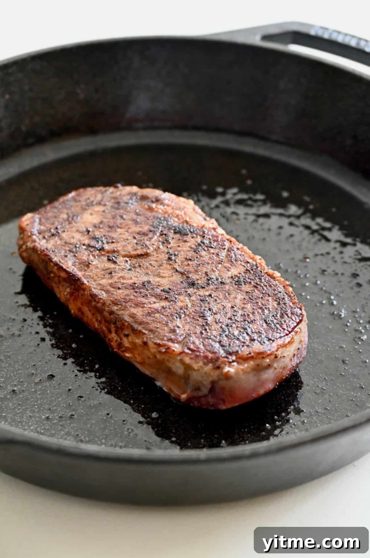 Searing the second side of a steak after flipping it in a hot cast-iron pan.