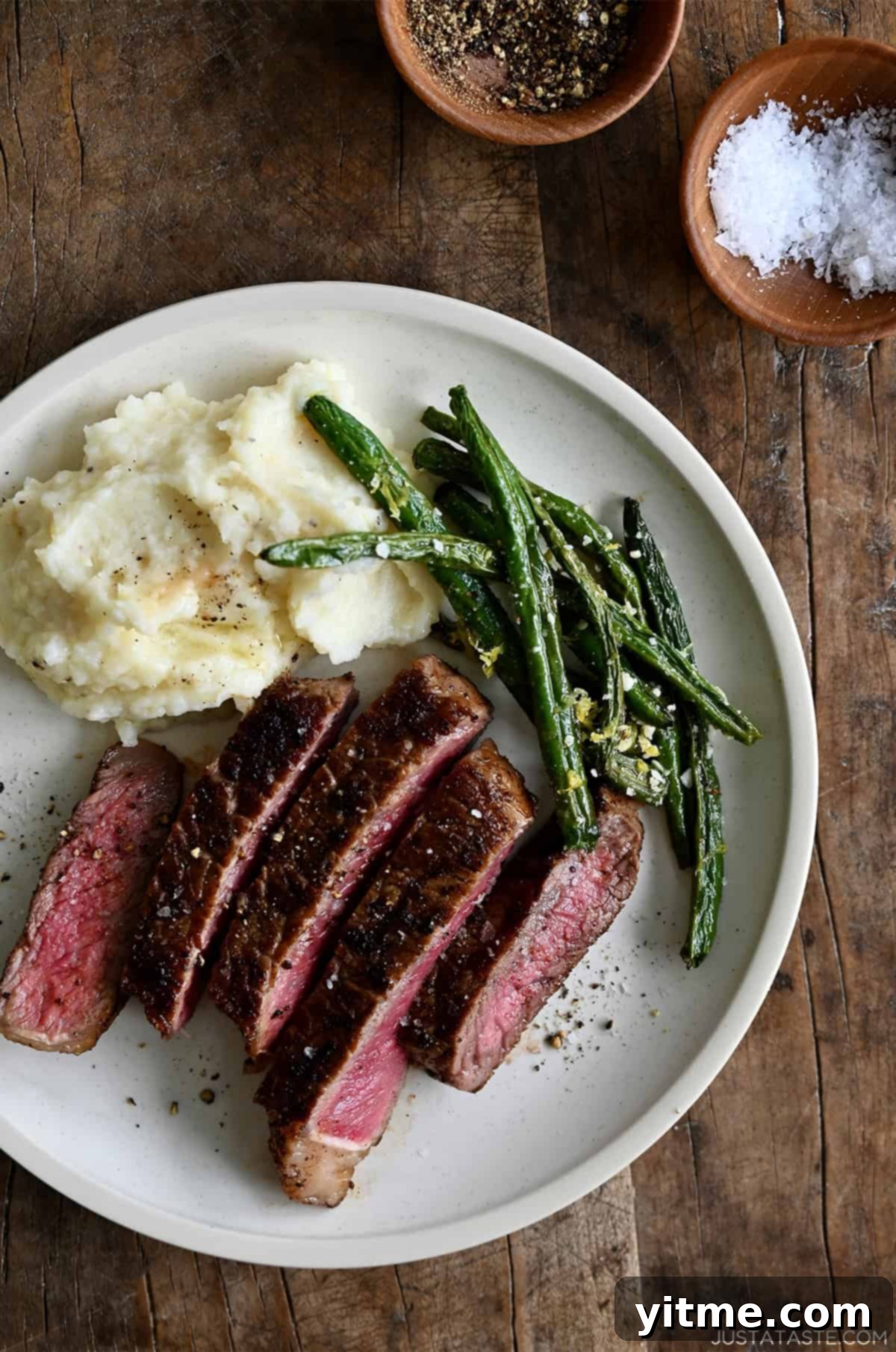 Sliced pan-seared steak served with blistered green beans and creamy mashed potatoes.