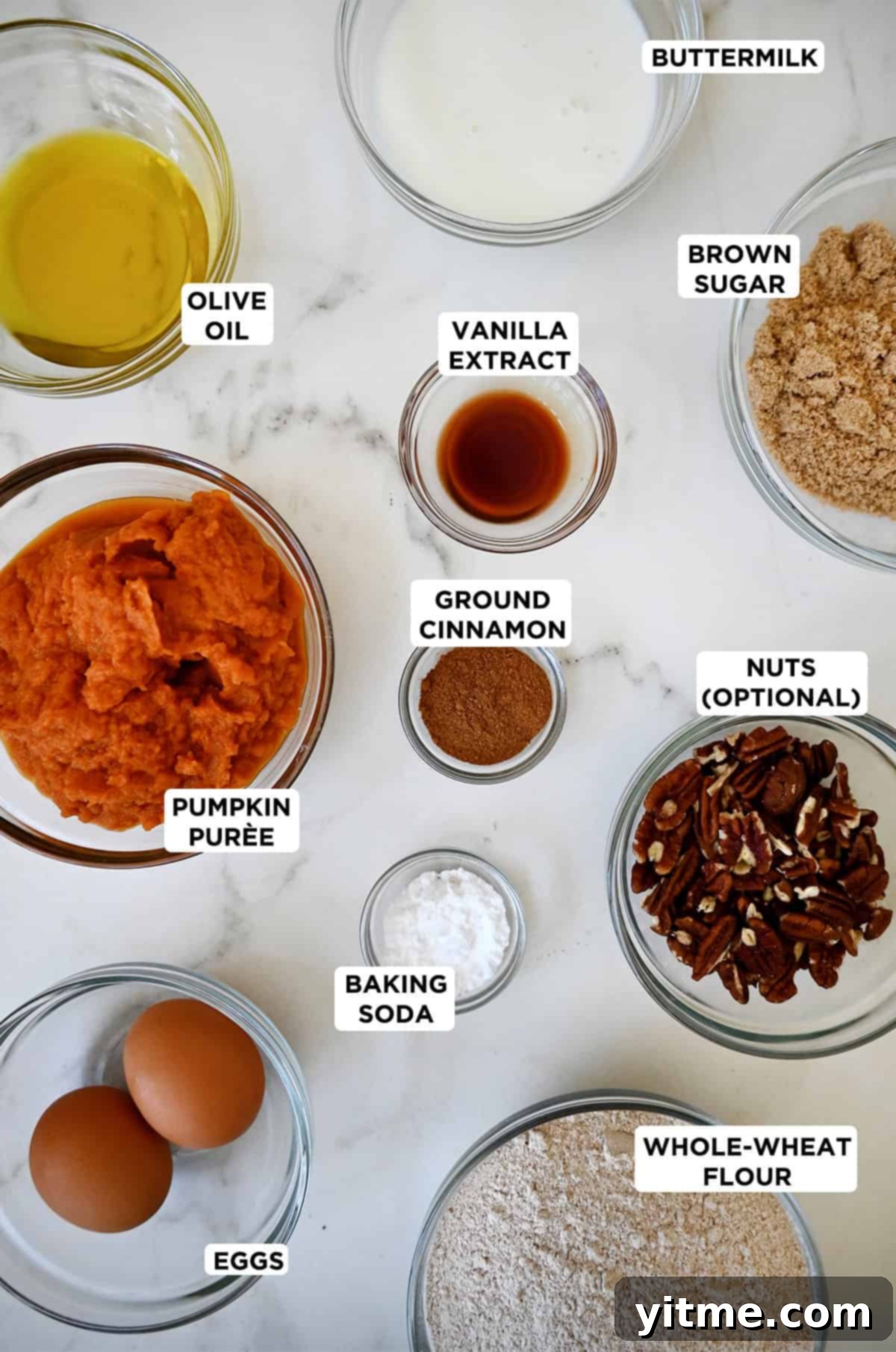 Wholesome Pumpkin Delights 4 A delightful assortment of ingredients needed for healthy pumpkin muffins, elegantly arranged in various sizes of glass bowls. The spread includes pumpkin puree, olive oil, brown sugar, vanilla extract, whole wheat flour, buttermilk, eggs, baking soda, pumpkin pie spice, and a generous helping of chopped pecans.