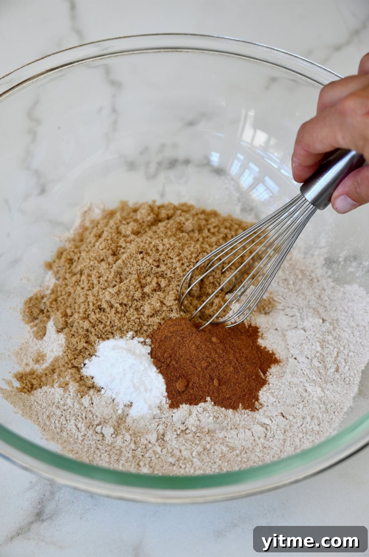 Wholesome Pumpkin Delights 5 A clear glass bowl showcasing the dry ingredients beautifully mixed together, ready to be incorporated into the pumpkin muffin batter. The mix includes pumpkin pie spice, whole wheat flour, baking soda, salt, and brown sugar.