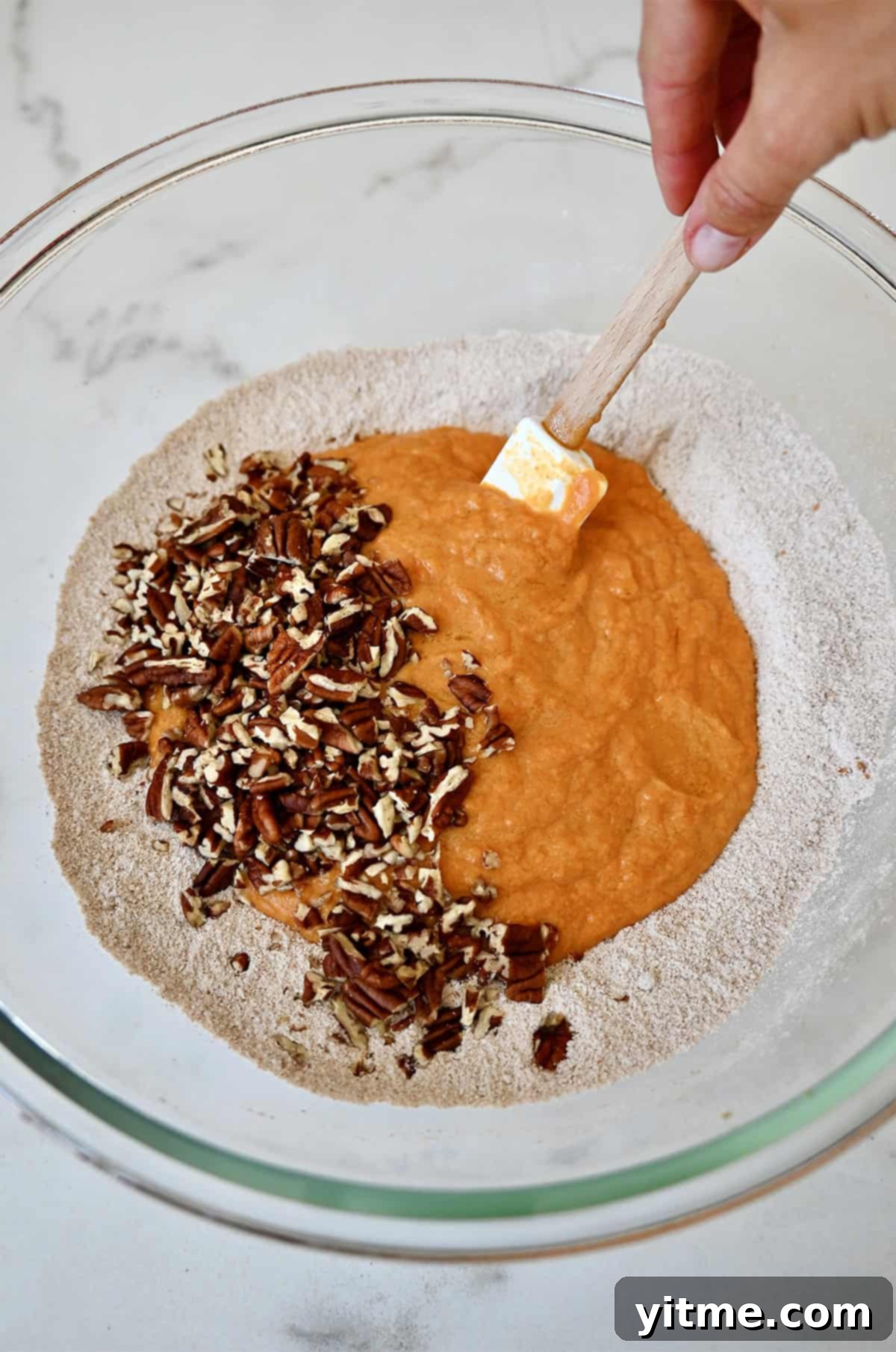 Wholesome Pumpkin Delights 7 Chopped pecans are being delicately folded into the pumpkin muffin batter in a mixing bowl. The combination of wet and dry ingredients creates a rich and inviting texture.