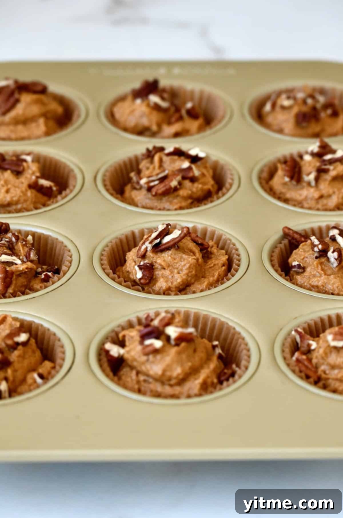 Wholesome Pumpkin Delights 9 A muffin tin lined with baking cups, each filled with healthy pumpkin muffin batter and topped with a sprinkle of chopped pecans, ready for the oven.