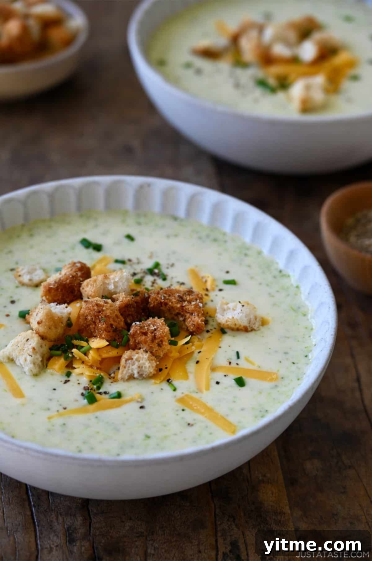Creamy Broccoli Cheddar Soup 2 A bowl containing creamy homemade broccoli cheddar soup topped with homemade croutons, chopped chives and shredded cheddar cheese.