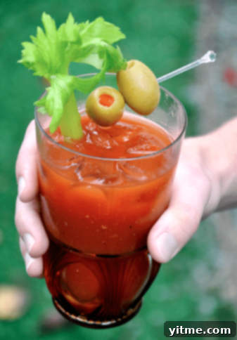 A festive pitcher of Bloody Marys for a Crowd, garnished with celery and olives, perfect for a Fourth of July brunch or party.