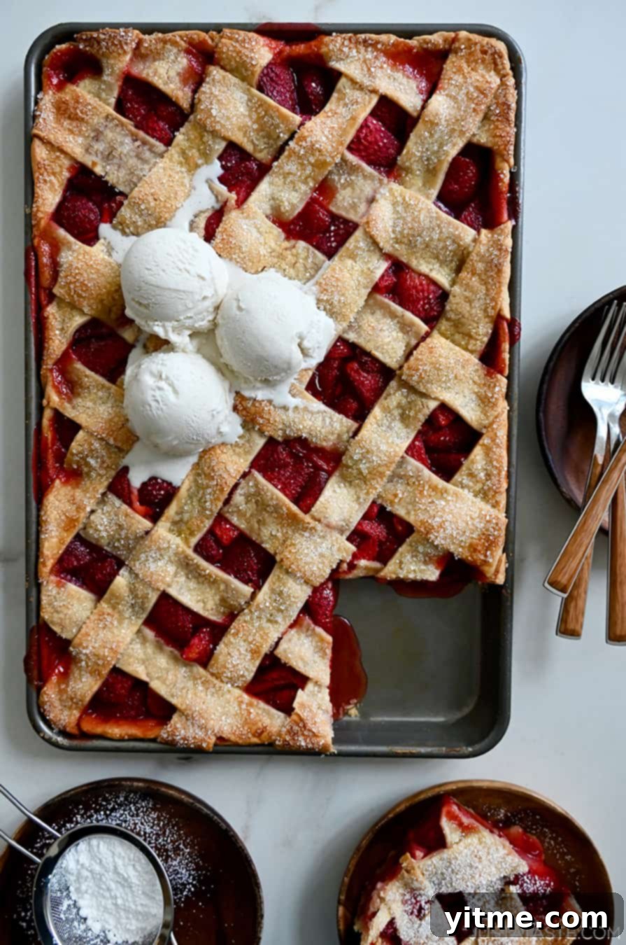 A top-down view of a Simple Strawberry Slab Pie topped with three scoops of vanilla bean ice cream, with a corner piece cut out and served on a plate next to it.