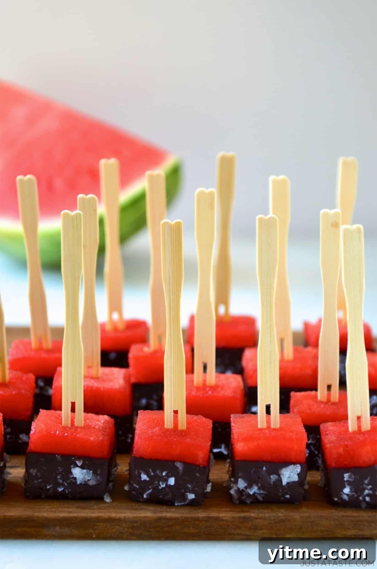 Frozen chocolate-covered watermelon bites with a sprinkle of sea salt and toothpicks on a serving plate, a healthy and refreshing summer snack.
