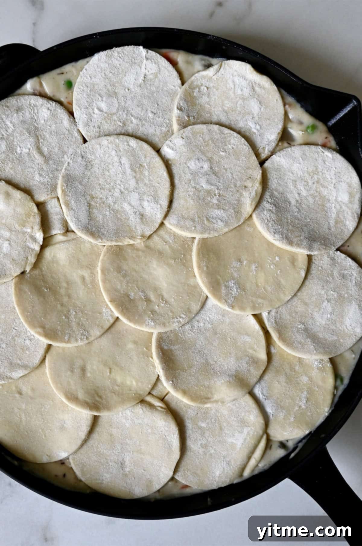 Adding puff pastry atop a skillet pot pie before baking.