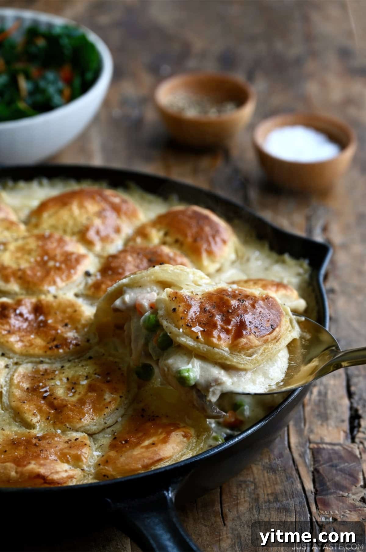 Scooping a serving of chicken pot pie from a cast-iron skillet, revealing the creamy filling loaded with chicken, veggies, and a golden puff pastry crust.