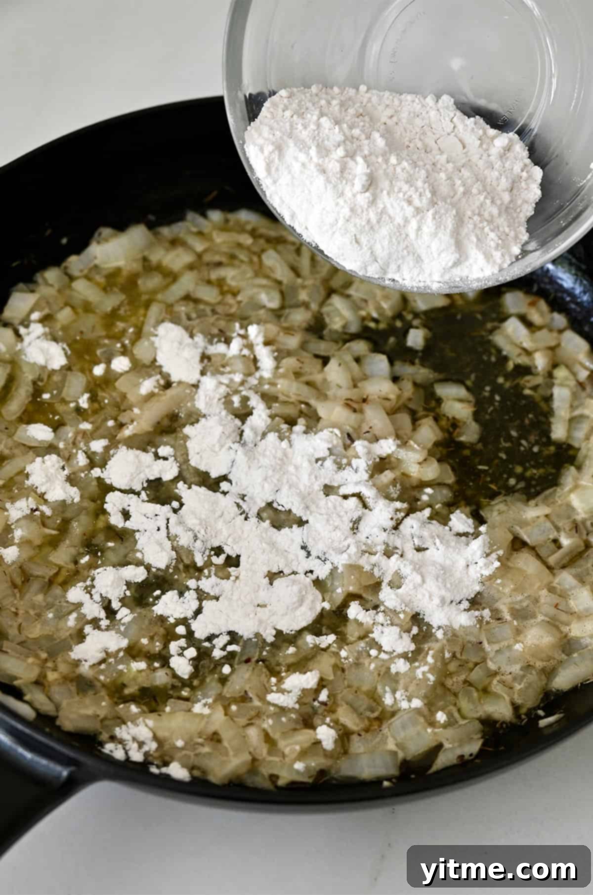Flour being stirred into butter and onions to form a roux for chicken pot pie filling.