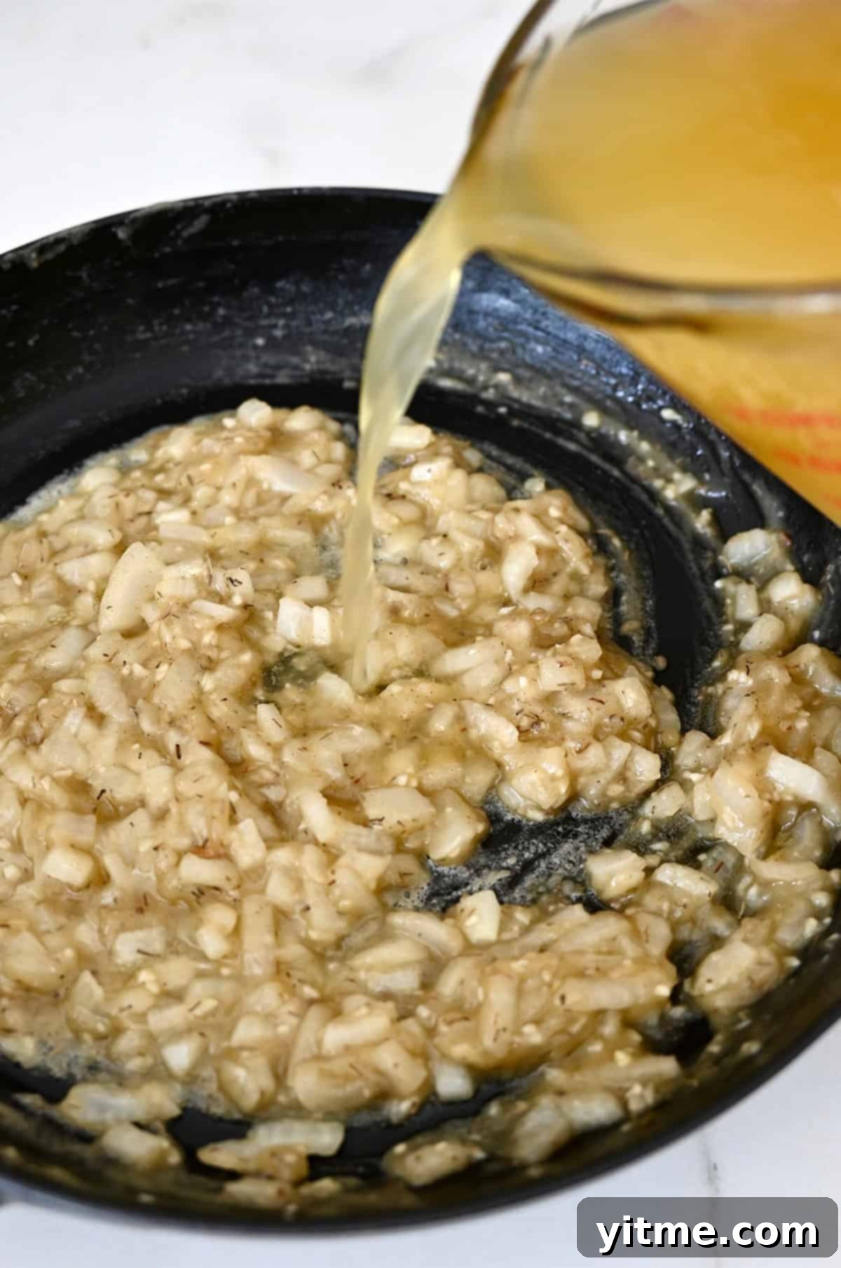 Adding chicken stock to a skillet with a roux.