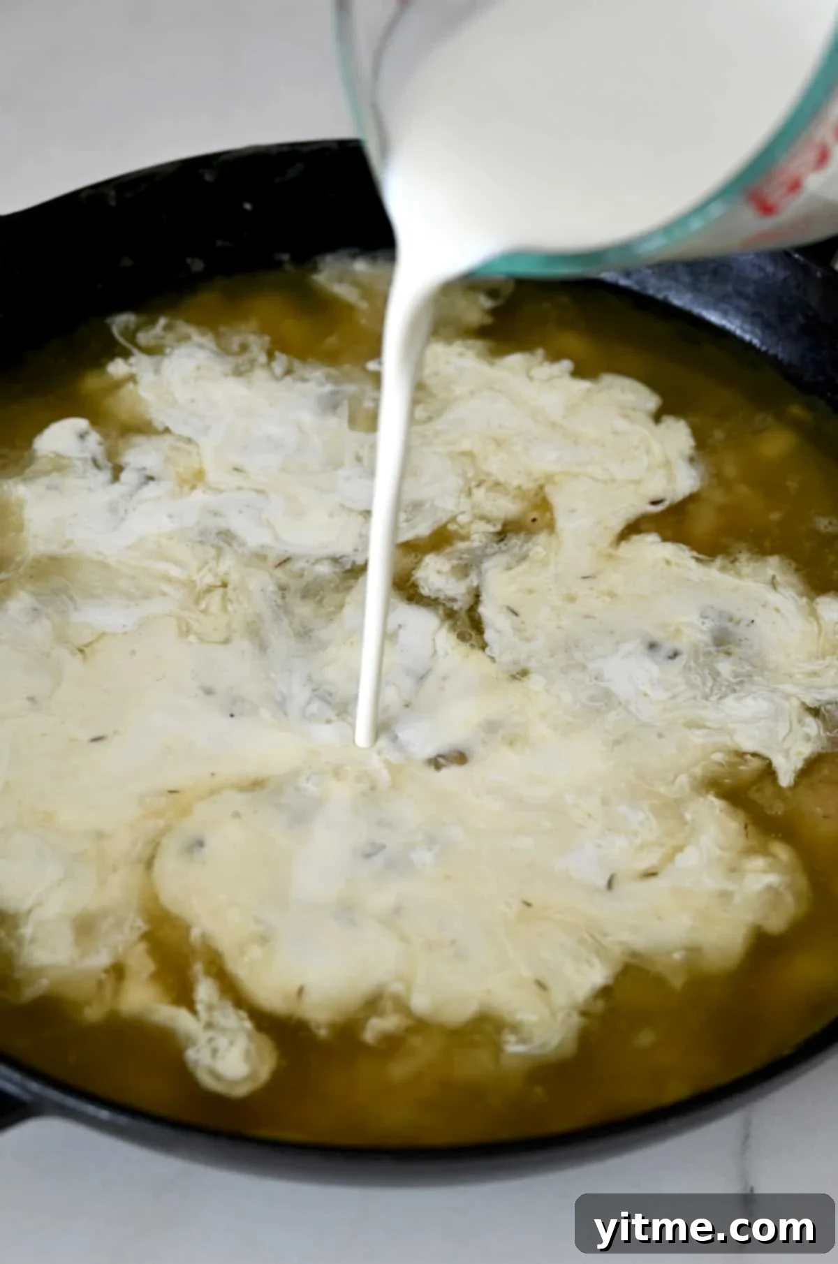 Adding heavy cream to a large skillet contianing a roux and chicken stock.