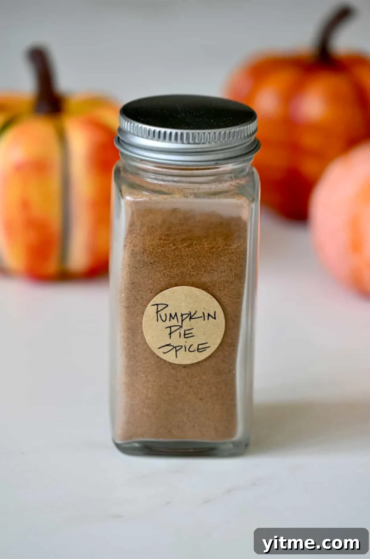 A charming glass spice jar, neatly labeled with 'Homemade Pumpkin Pie Spice,' sits on a rustic wooden surface, ready to infuse your recipes with autumn flavor. The focus is on the rich, warm color of the spice within the jar, hinting at its aromatic depth.