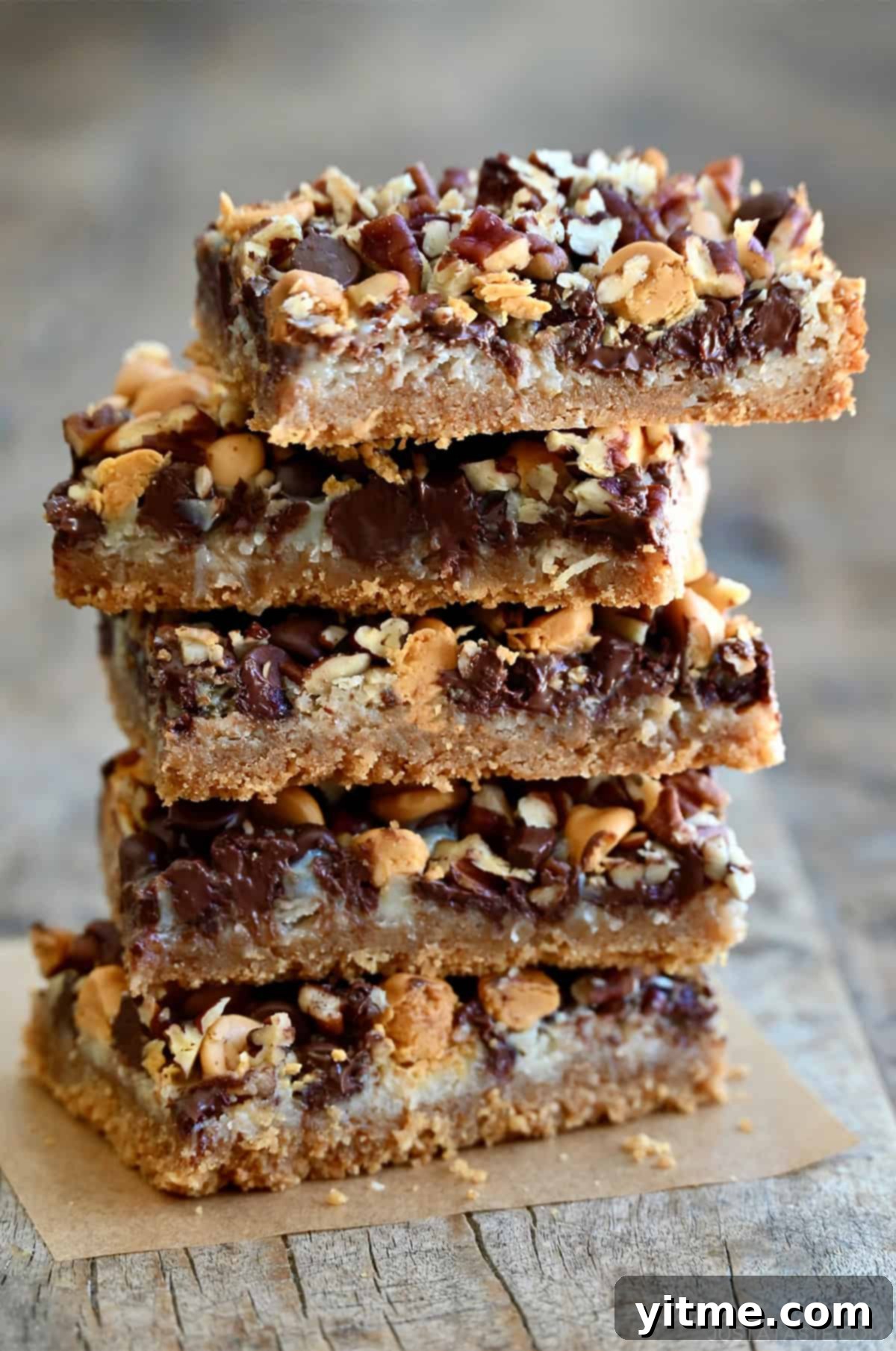 Everything Cookie Bars 2 Magic cookie bars stacked five high on a piece of parchment paper, showcasing their delicious layers and golden-brown top.