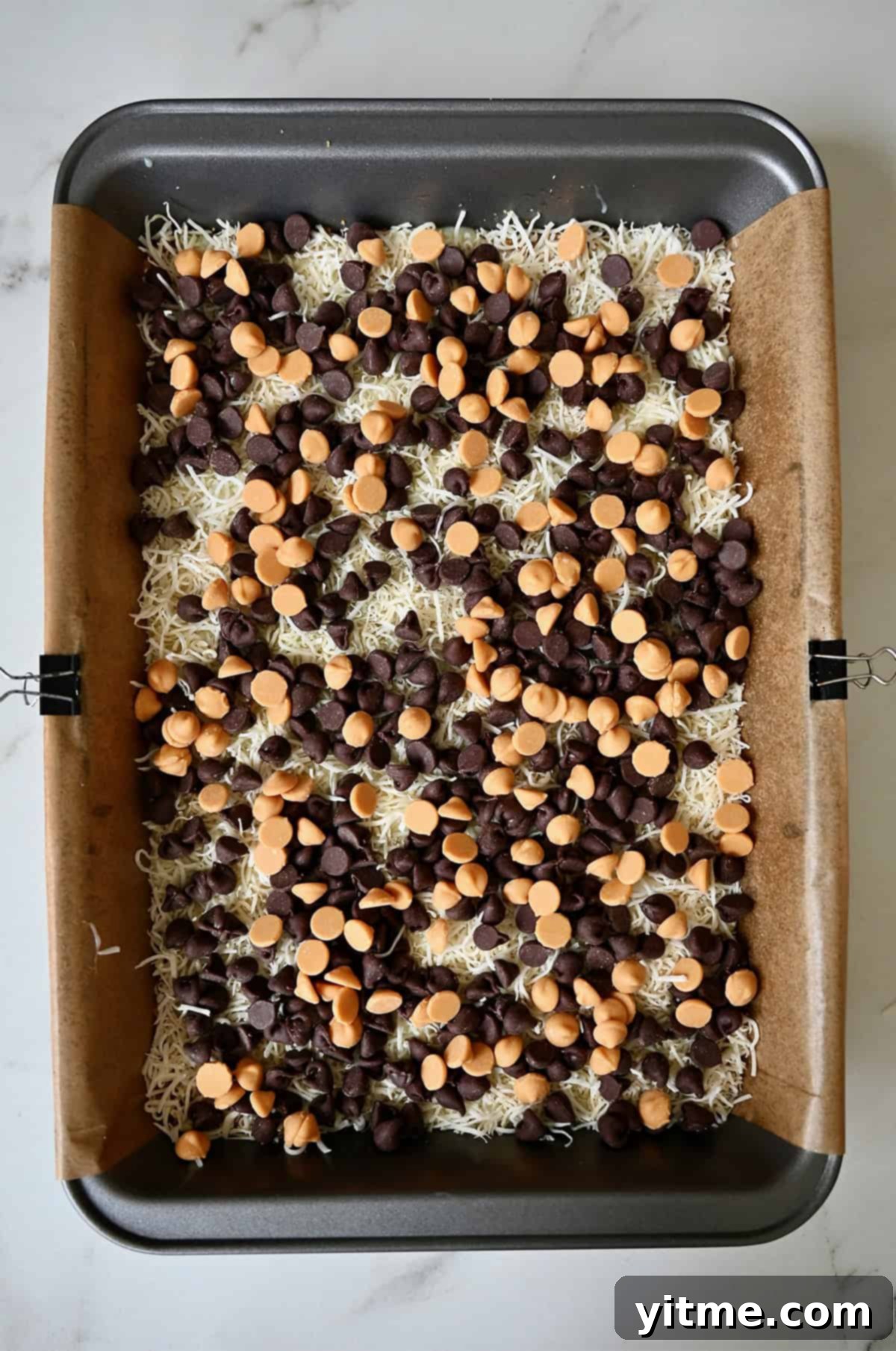 Everything Cookie Bars 12 Adding a layer of butterscotch chips on top of chocolate chips and coconut for 7-layer bars, completing the sweet layers.